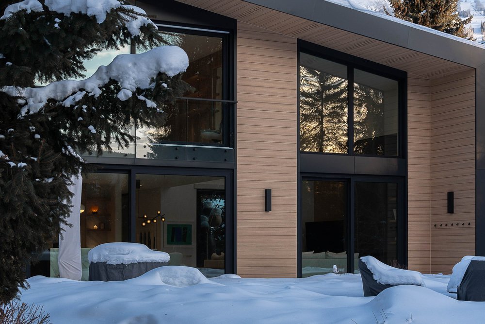 Rear elevation in low sun, snow over the terrace furniture and warm light inside