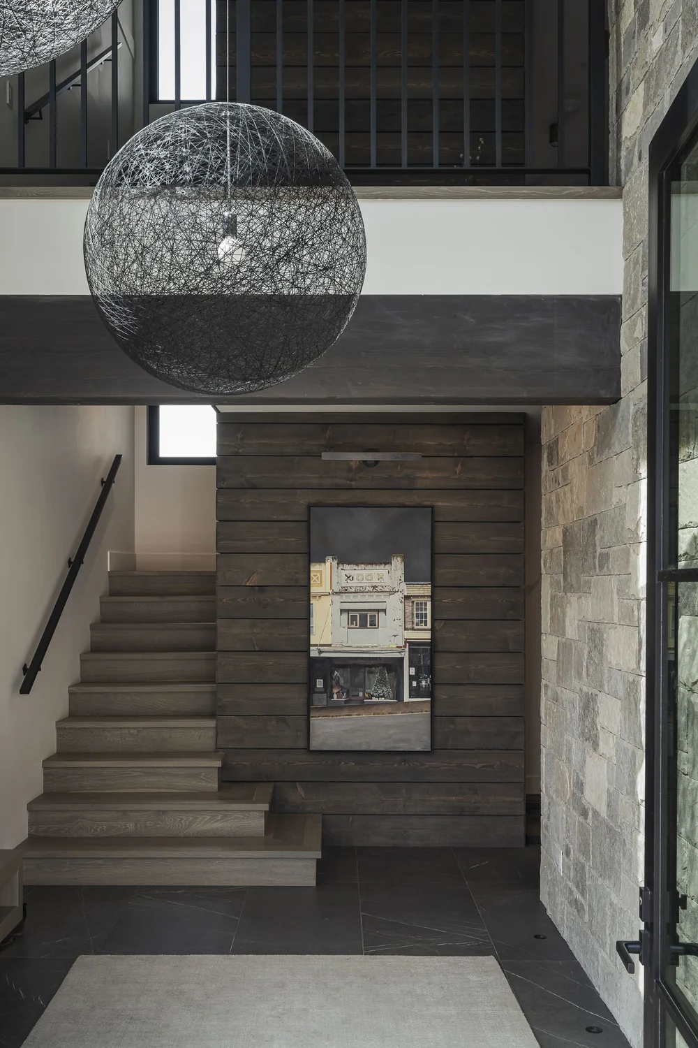Stair from the entry under a large woven sphere pendant, dark wood wall beyond