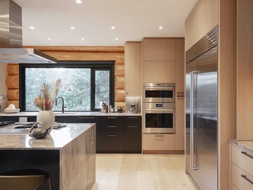 Kitchen from the far end, the island in front of wall ovens and a tall refrigerator