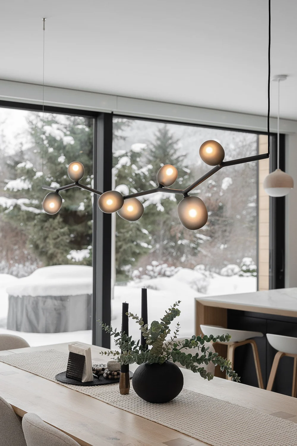 Amber globes on a branching pendant above the dining table, snowy trees at the window