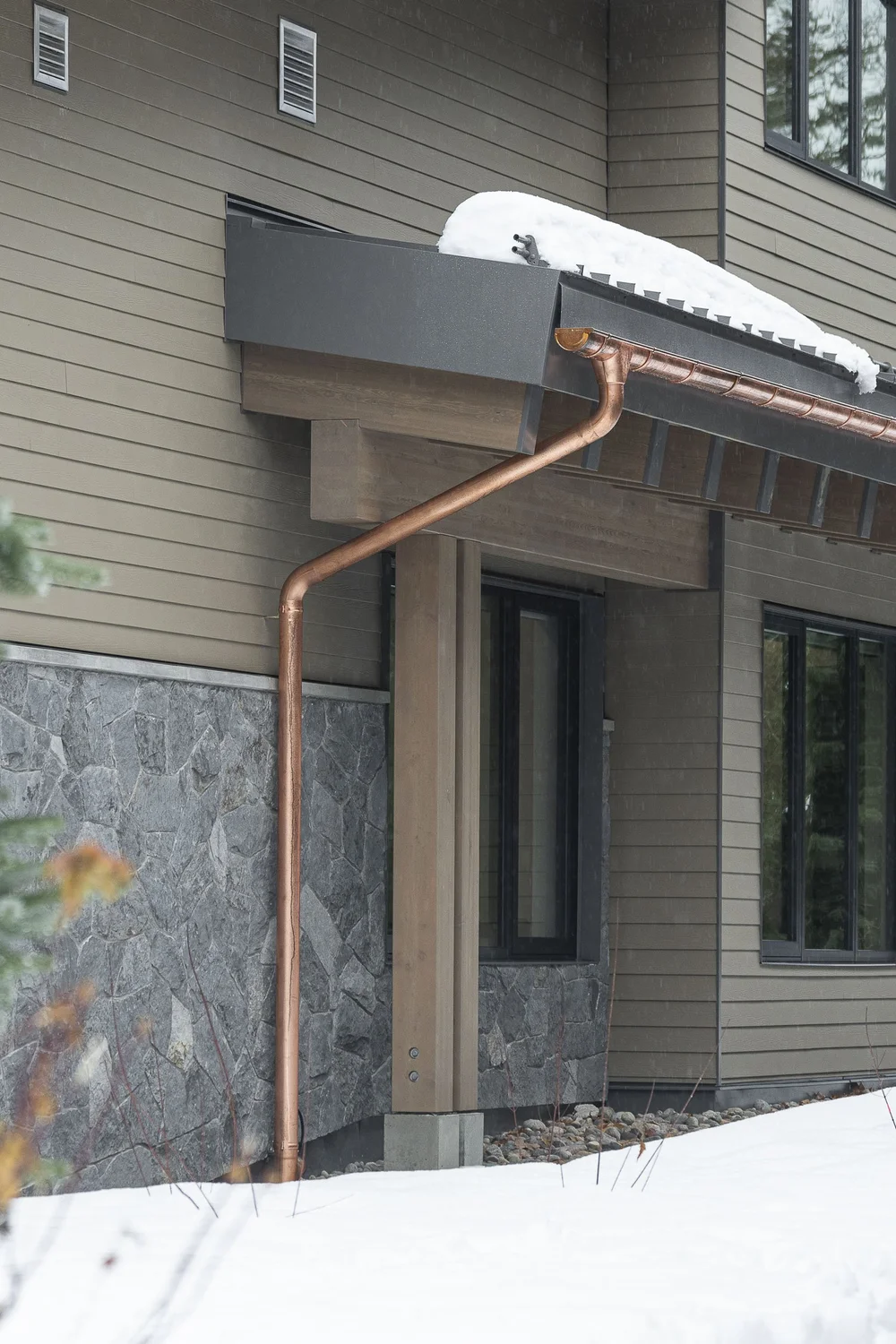 A copper downspout running down siding to a stone base beside a covered entry