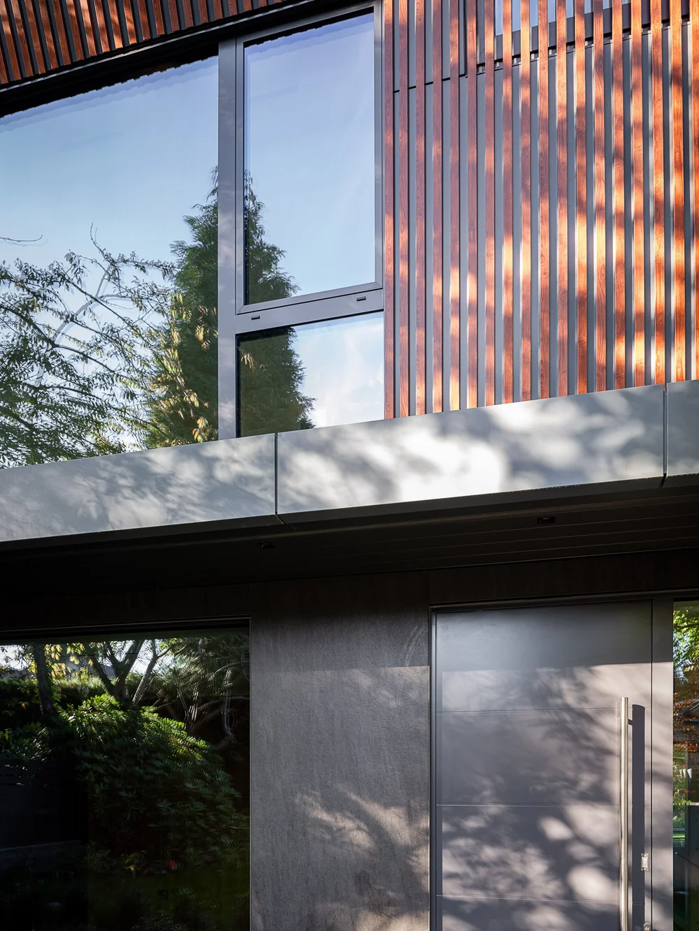 Upper window and wood slat cladding above the entry, shadows across the panels