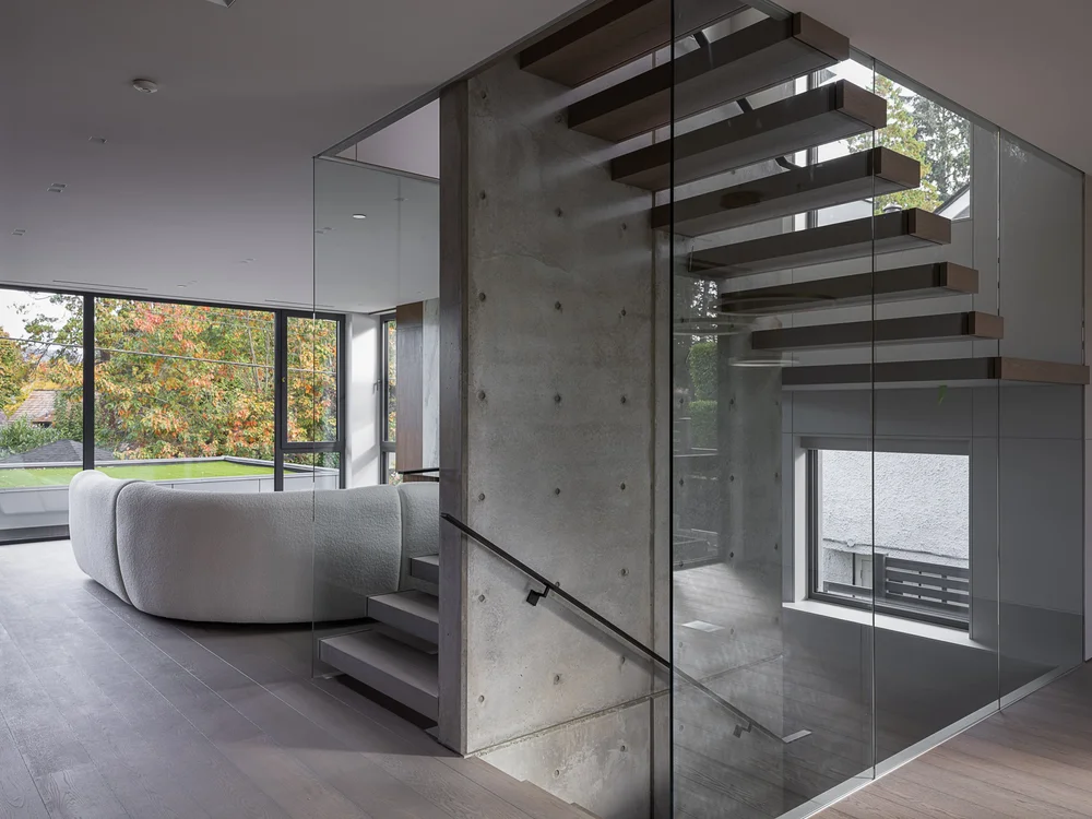 Living room past a concrete wall, floating treads behind glass and a curved sofa