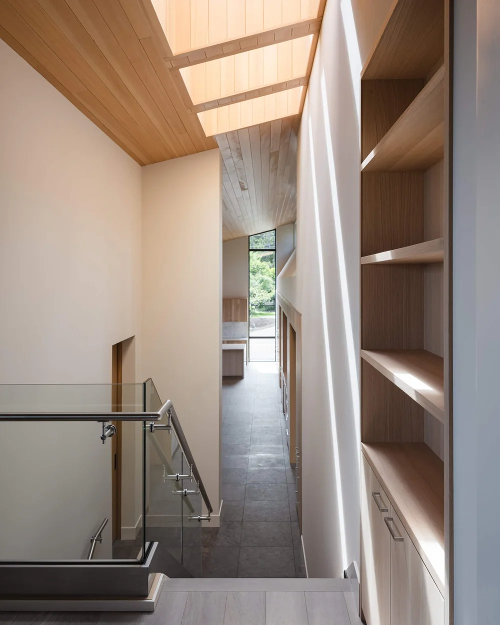 Upper hall under a run of skylights, tall shelving to one side and a glass balustrade