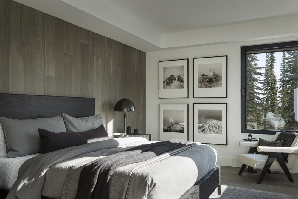 Bedroom with four framed prints beside the bed, window onto tall evergreens