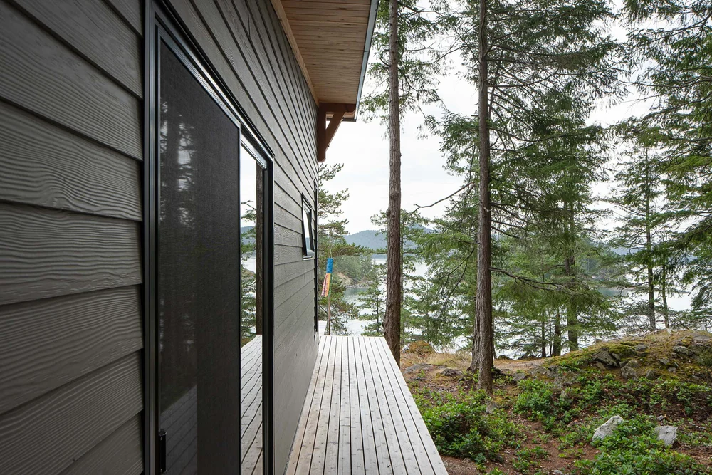 Looking along the lap siding and a dark screen door, deck boards running to the water