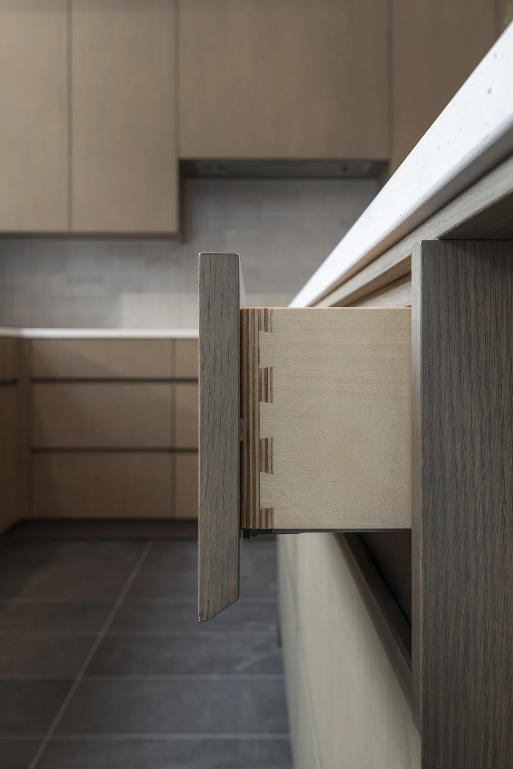 An open cabinet panel showing its joined edge against dark fronts and a tile floor