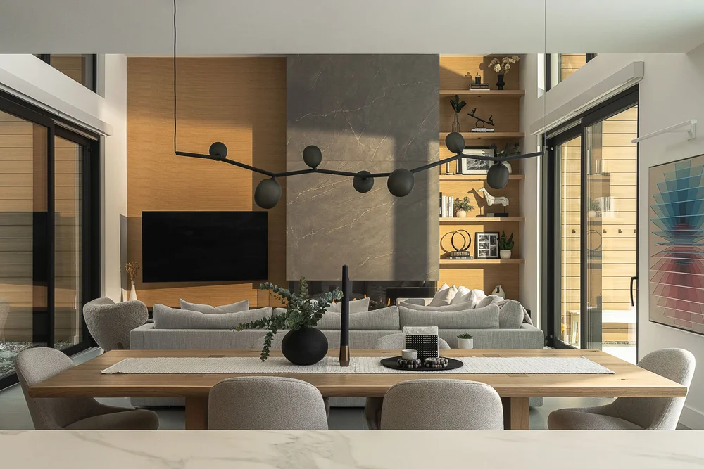Dining table under a branching pendant, the living room and full height glazing beyond