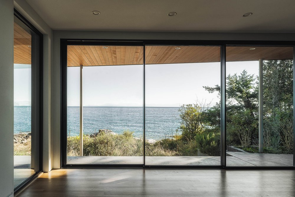 The house from below a rock wall, two storeys of glazing under a wood soffit, forest behind