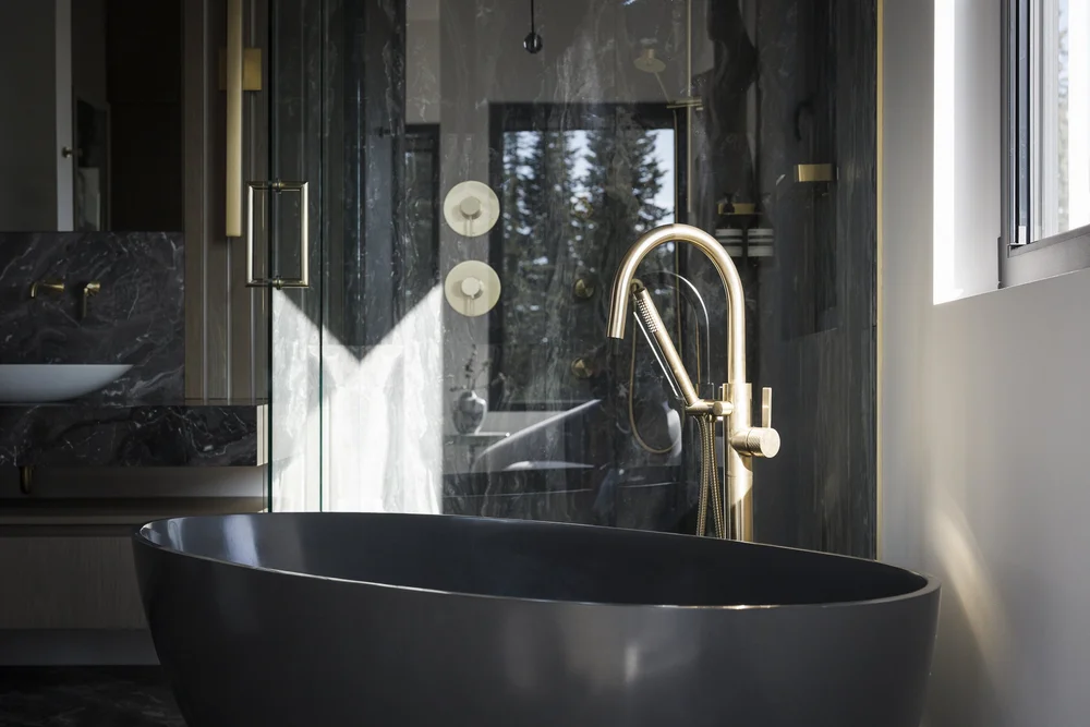 Dark tub and a glass shower in a bathroom lined with dark stone