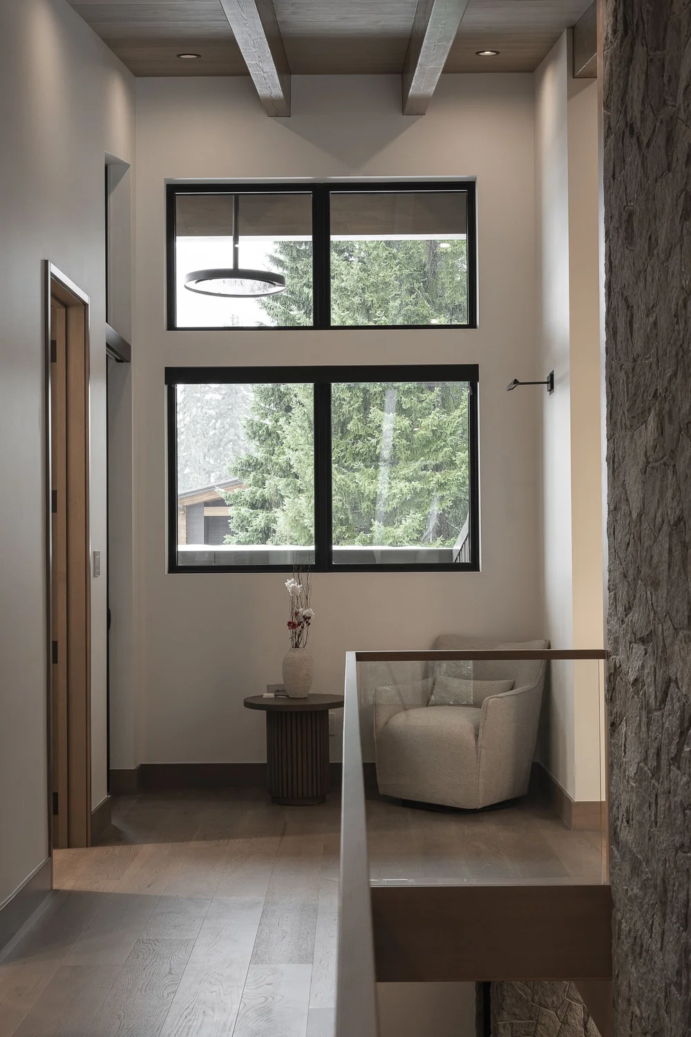 Hallway under dark ceiling beams to a window, a chair and round table at the end
