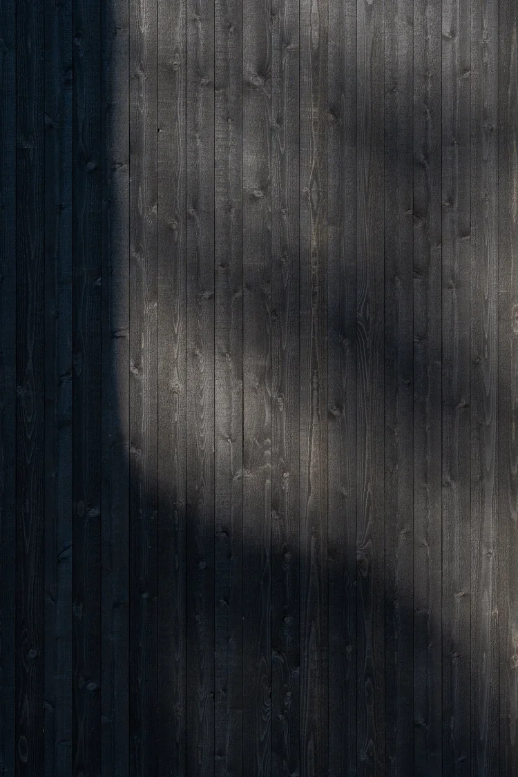 Dark stained wood siding with a tree shadow