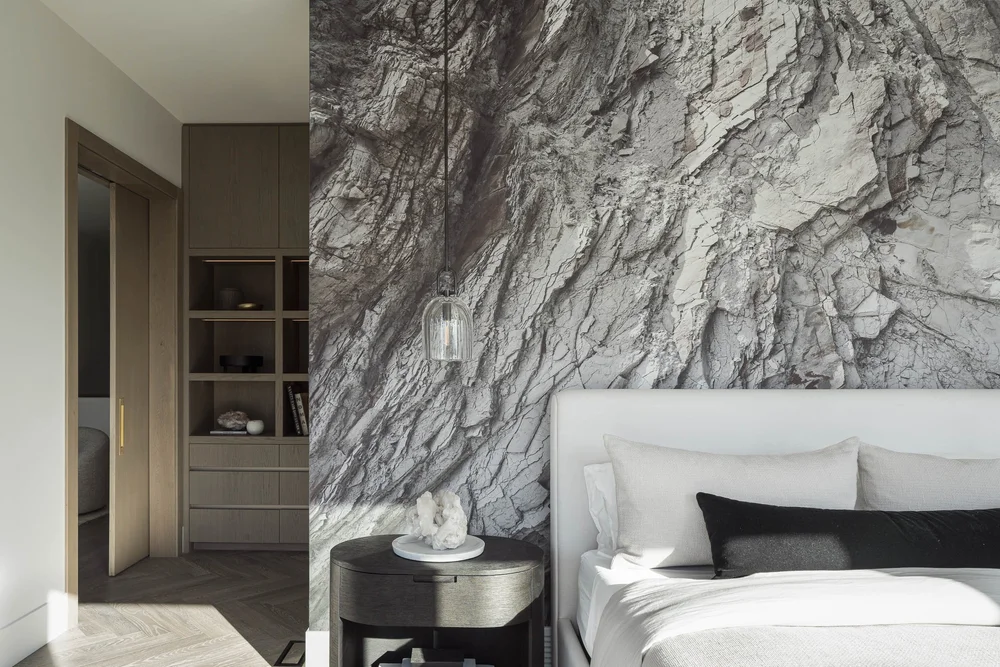 Bed against a wall of heavily veined stone, glass pendant hanging beside it