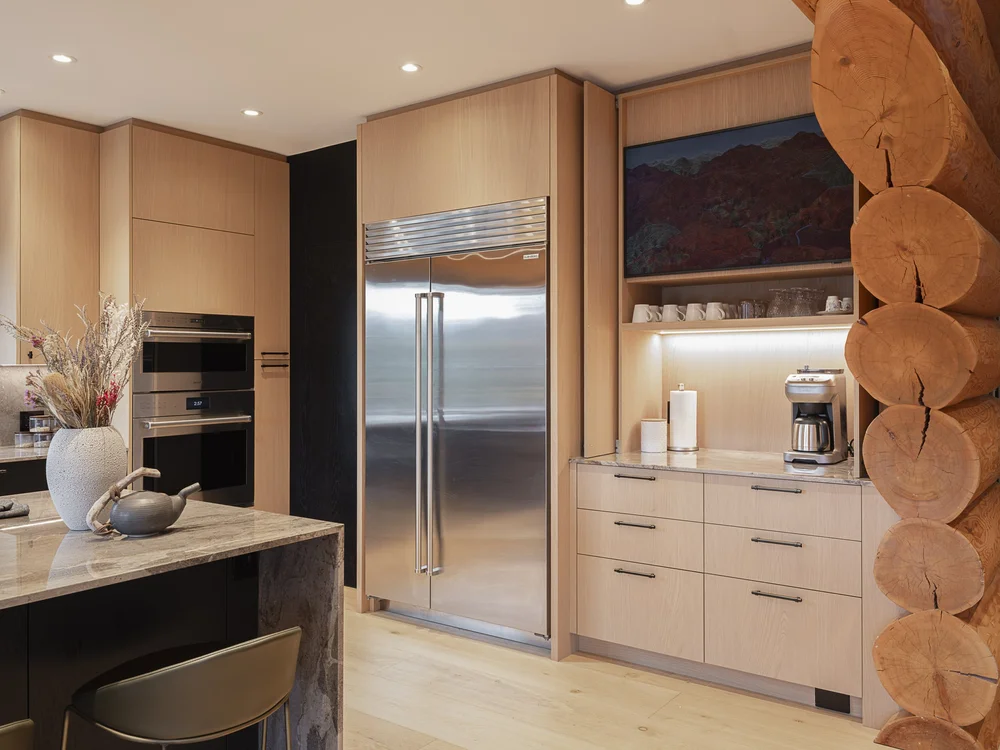 Refrigerator and wall ovens set into pale cabinetry, a framed landscape above the counter
