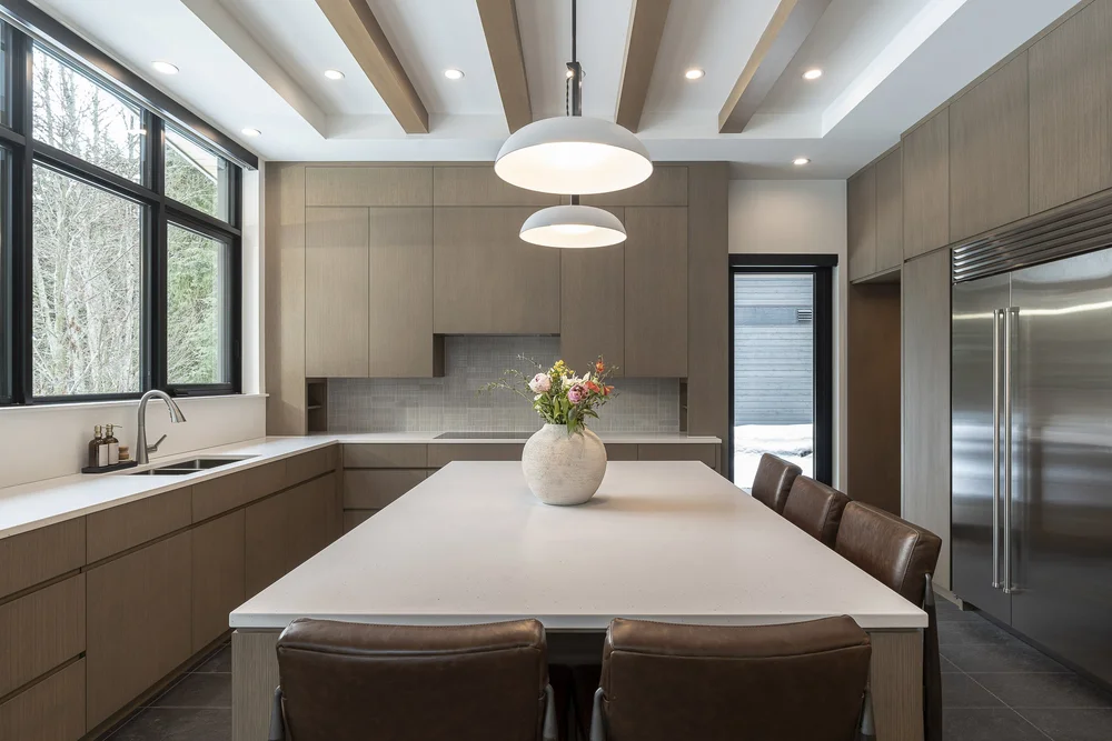 Kitchen with a long pale island, brown upholstered stools and dome pendants under exposed beams