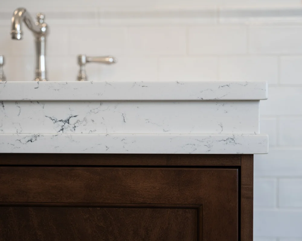 A thick white veined counter with a shaped edge above dark wood, white tile behind