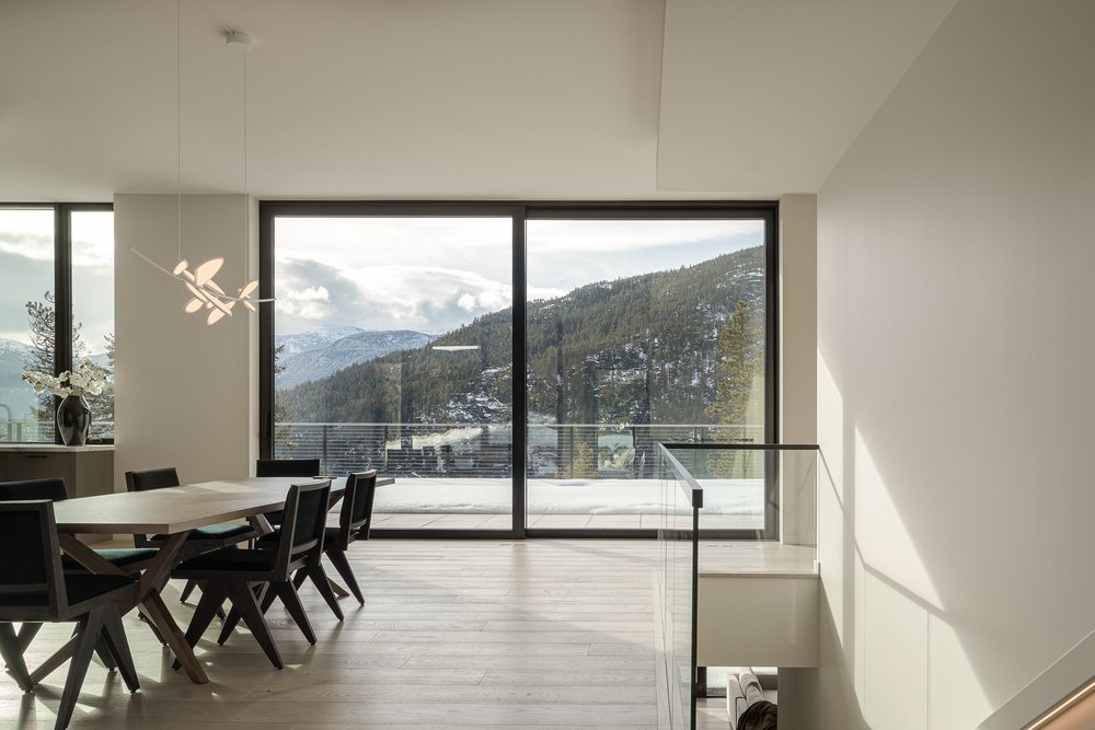 Dining table and chairs under a branching pendant, full height glazing to the mountains