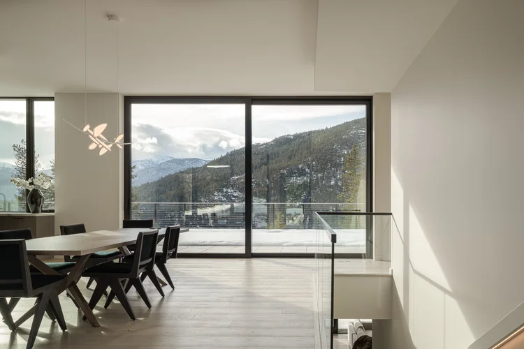 Dining table and chairs beside a glass wall with a snow covered mountain beyond