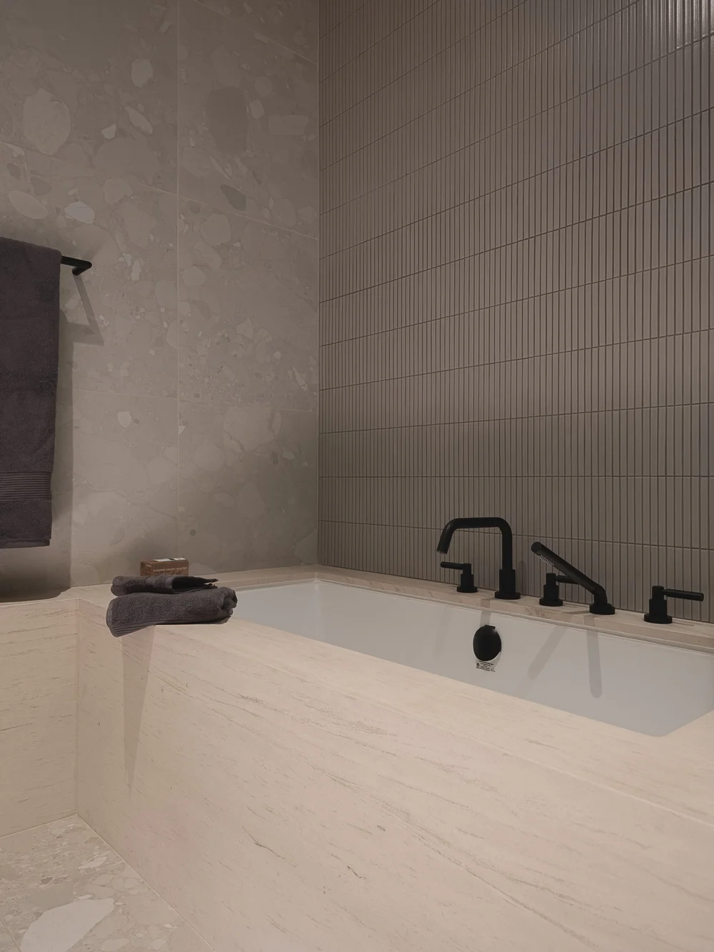 Undermount tub in a stone lined alcove, black taps and a folded dark towel