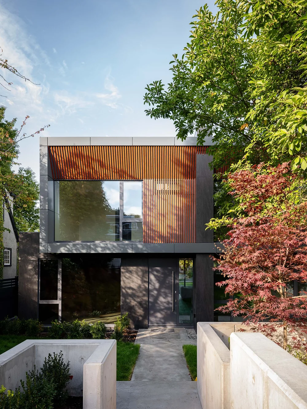 The front elevation seen straight on between trees, a concrete path to the entry