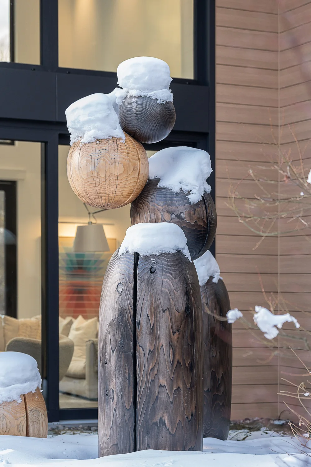 Carved wood sculptures capped with snow outside the glazing, a lit room behind