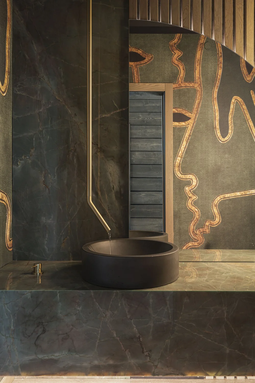 Powder room in dark stone with copper coloured veining, round basin below a lit mirror