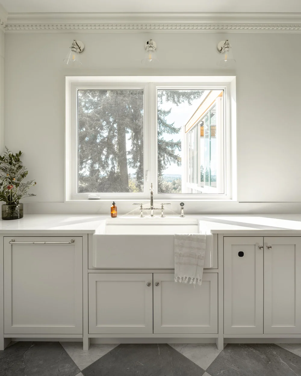 An apron sink below a corner window, three sconces above and cream cabinetry either side