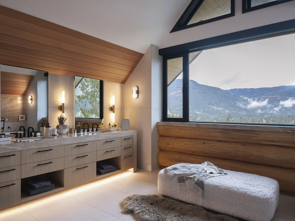 Vanity and mirror below a wood plank ceiling, mountains through the window beyond