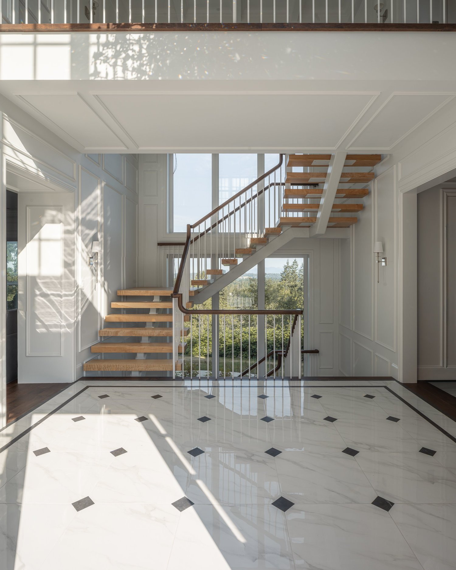 Entry hall in polished pale tile with black diamond inserts, the open stair beyond
