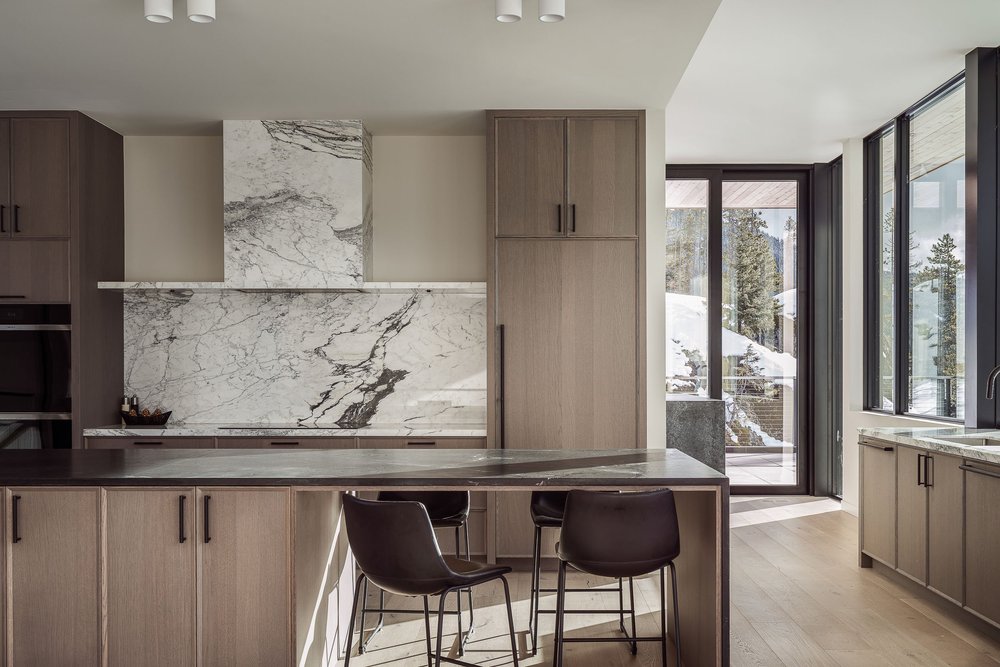 Kitchen with a veined stone backsplash, pale timber cabinetry and a dark stone island