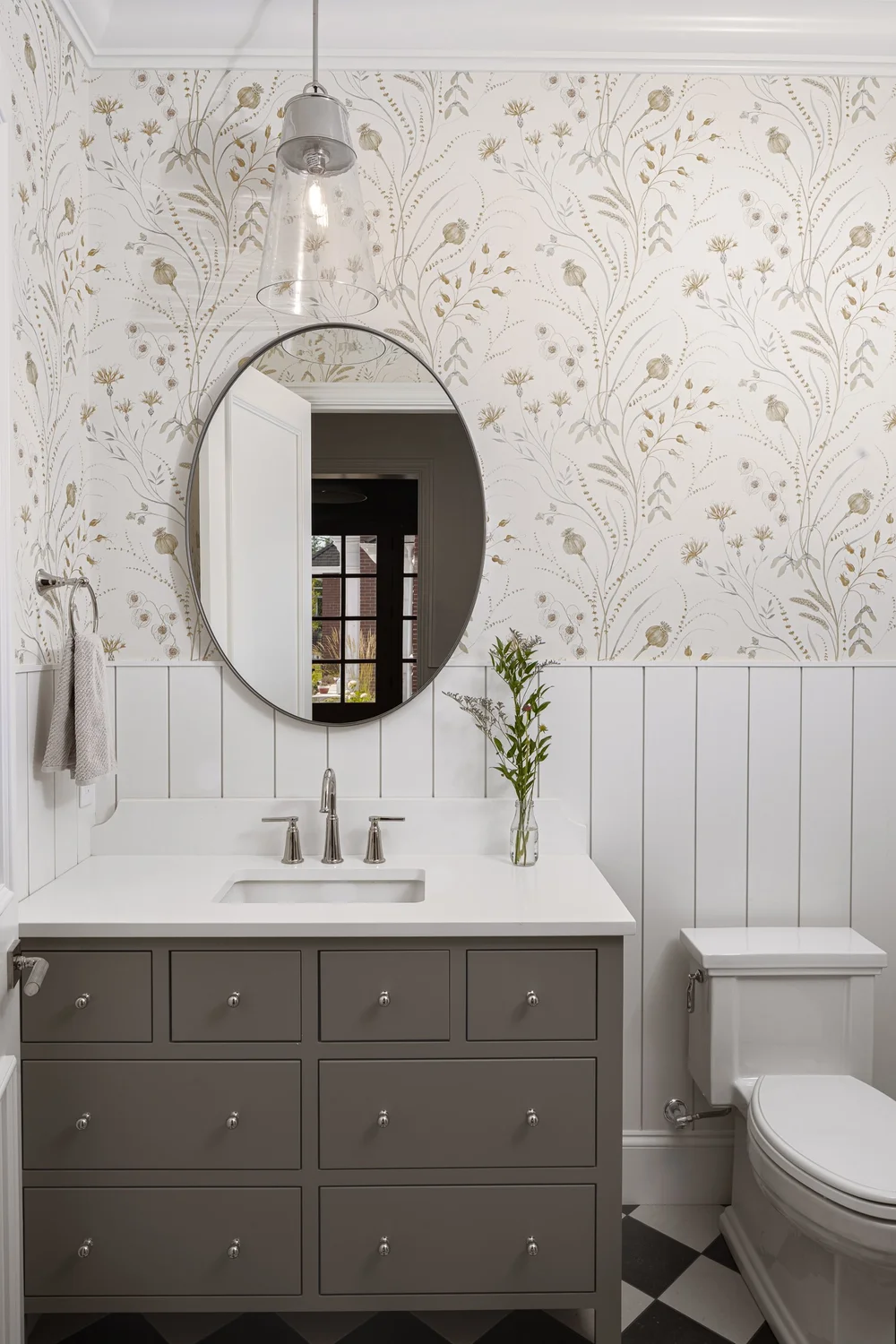 Powder room with floral wallpaper above white boarding, an oval mirror over a taupe vanity