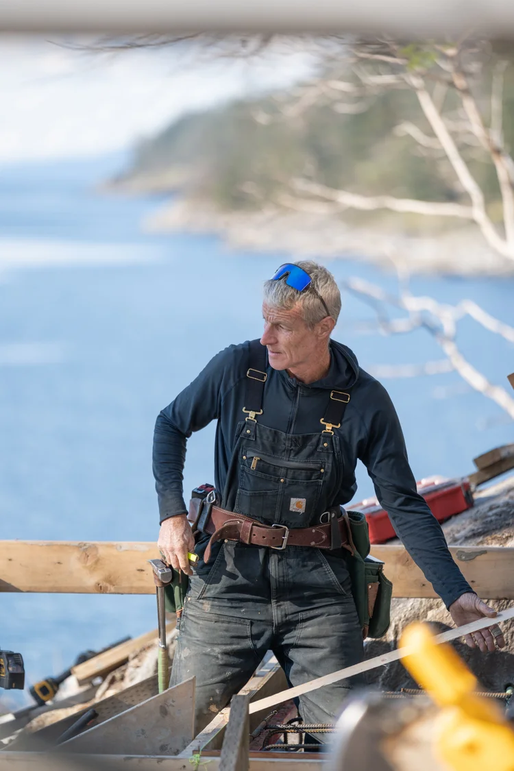 Builder in overalls with a tool belt, ocean behind