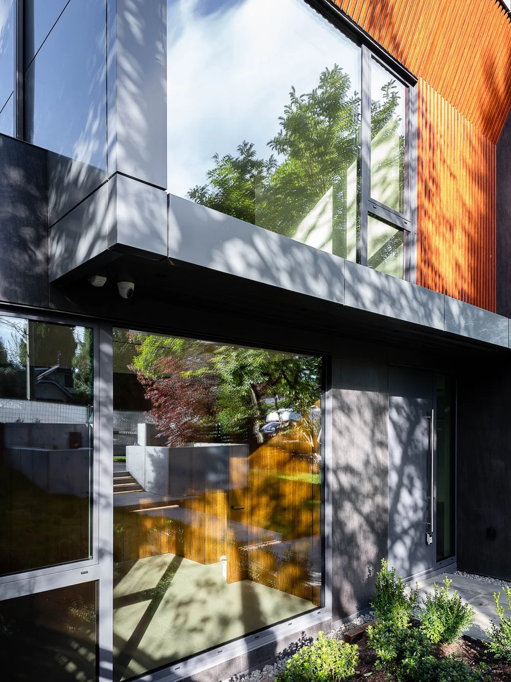Glazing and a cantilevered upper storey in dappled shade, wood slats along the flank