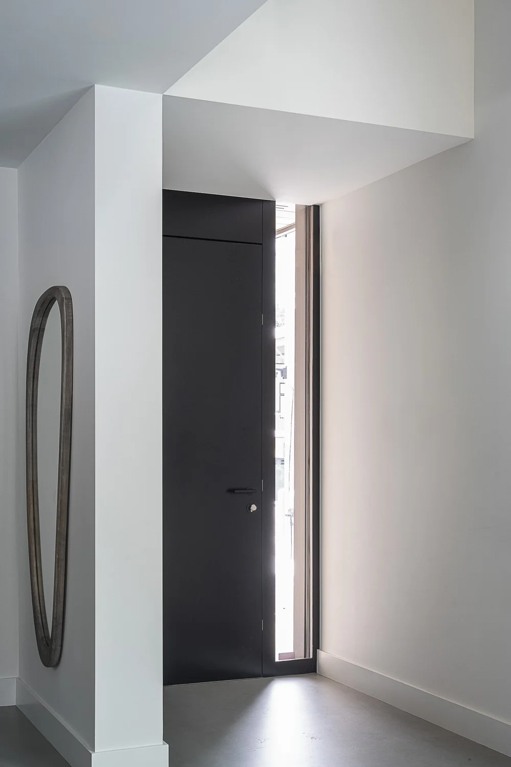 Entry hall with a dark flush door, a tall slot window and an oval mirror