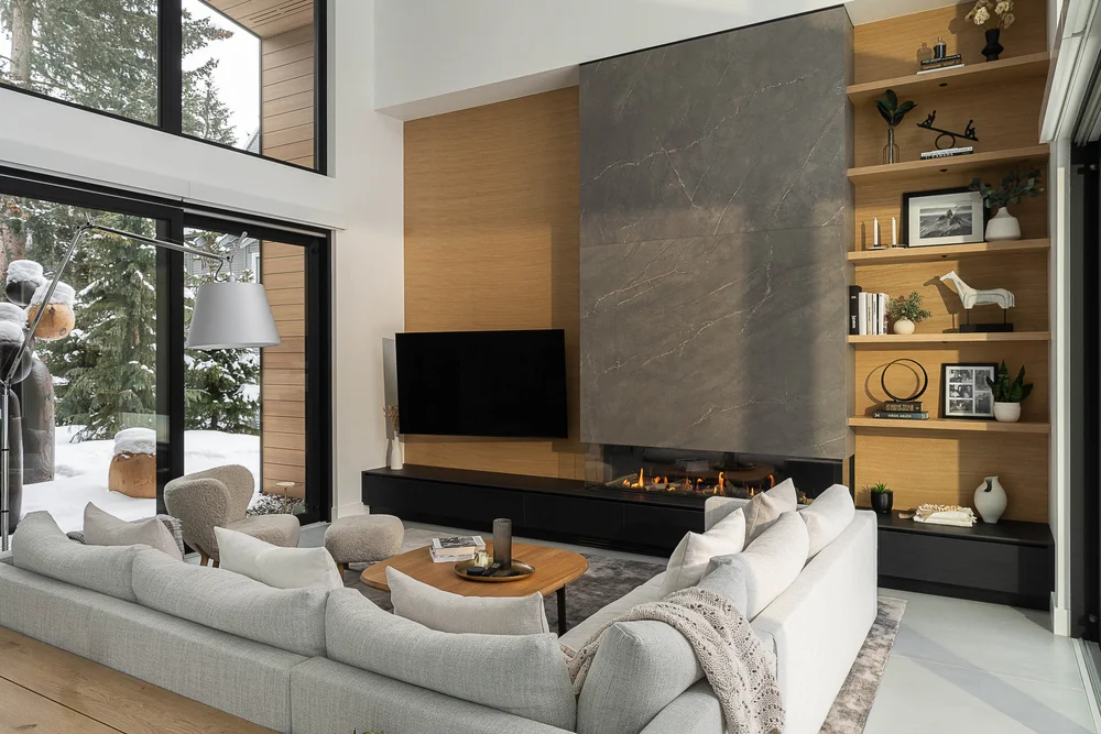 Living room with a dark stone fireplace wall, a pale sectional and glazing onto the snow