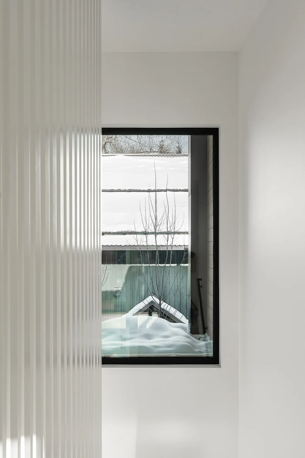Fluted glass panel beside a black framed window looking onto deep snow outside