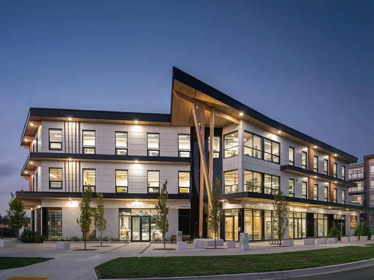 The building from the corner at dusk, every floor lit behind glass above the lawn