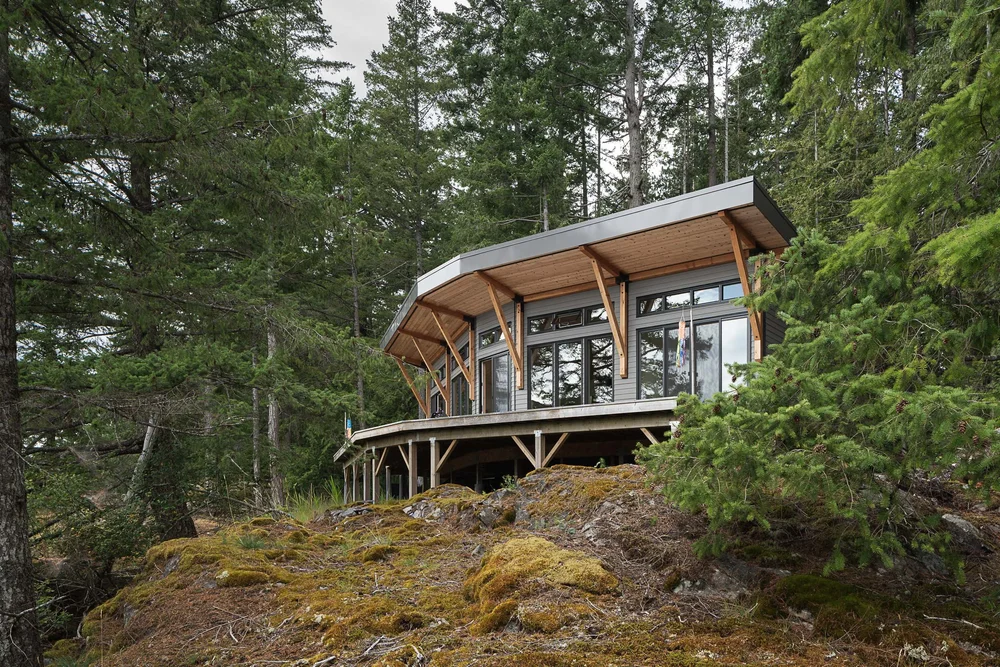 The house on a moss covered rock outcrop, its deck on posts above the drop