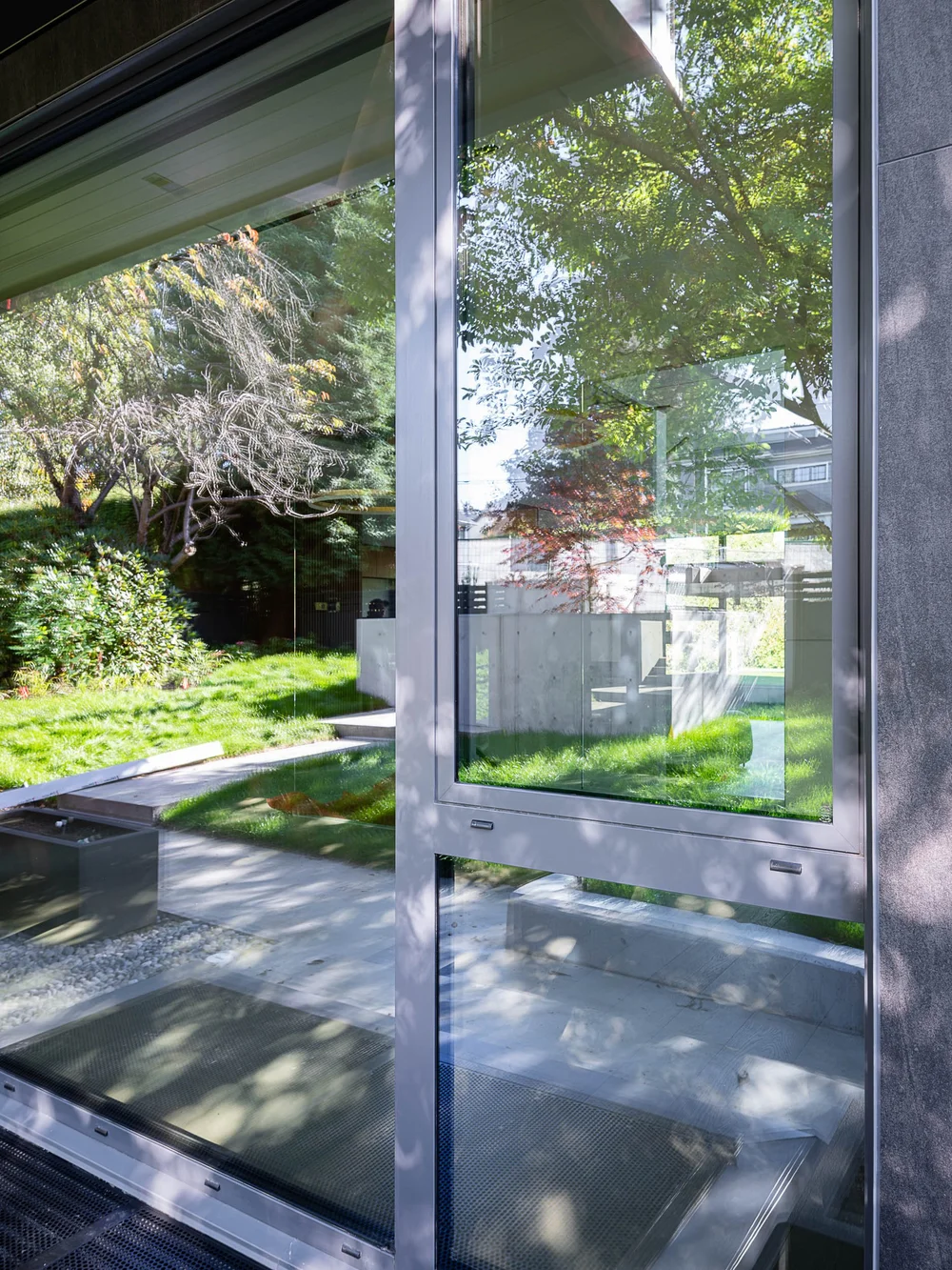 Corner glazing beside the entry, garden and concrete steps doubled in the reflections