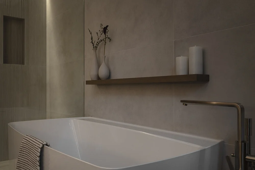Freestanding tub against large format tile, a shelf above with a vase and two candles
