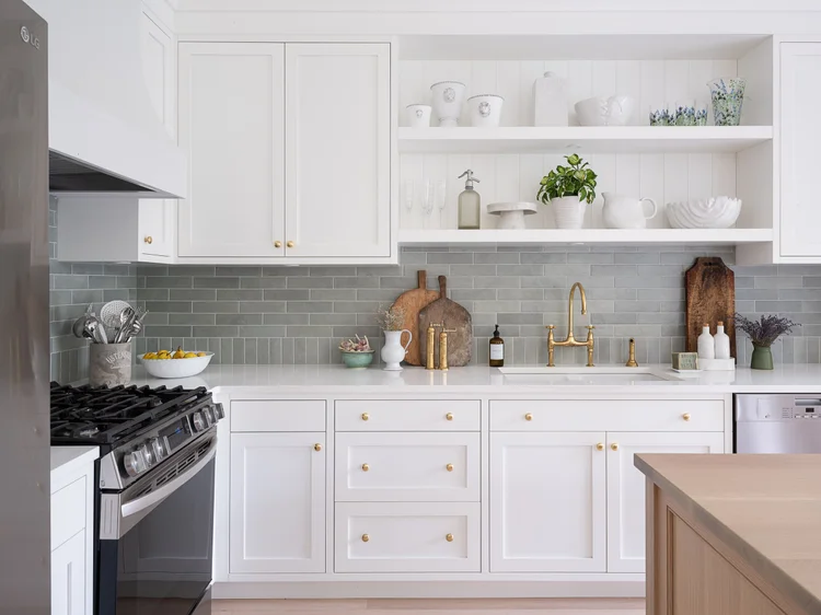 White shaker kitchen with a green tile backsplash, brass fixtures and open shelving