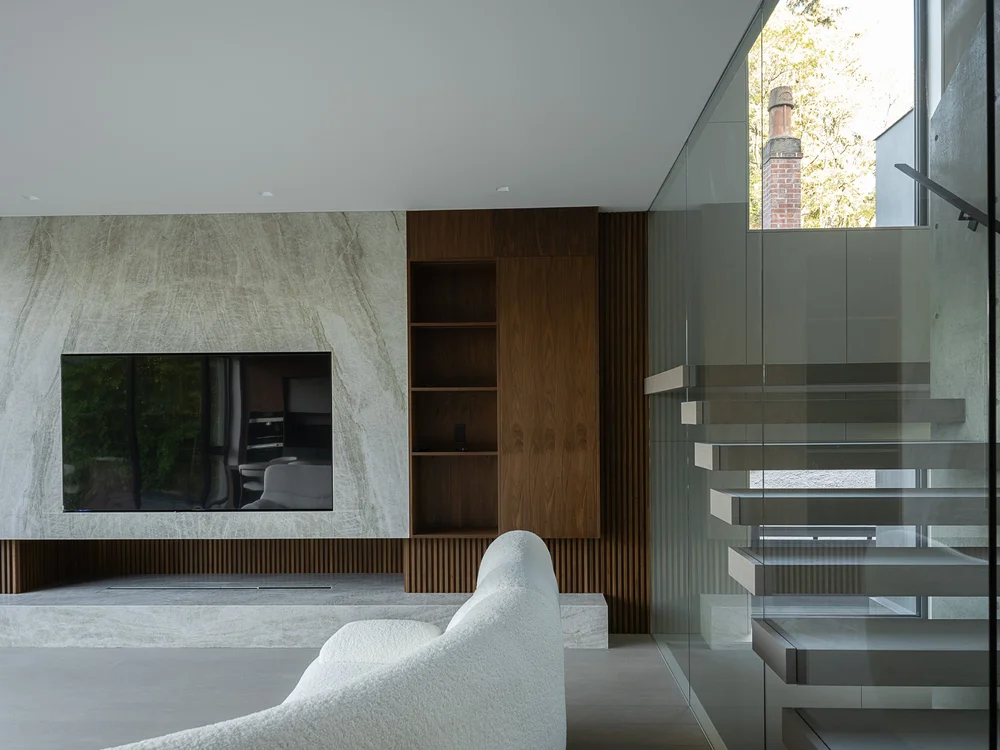 Living room with a veined stone fireplace wall, timber shelving and the glass stair beyond