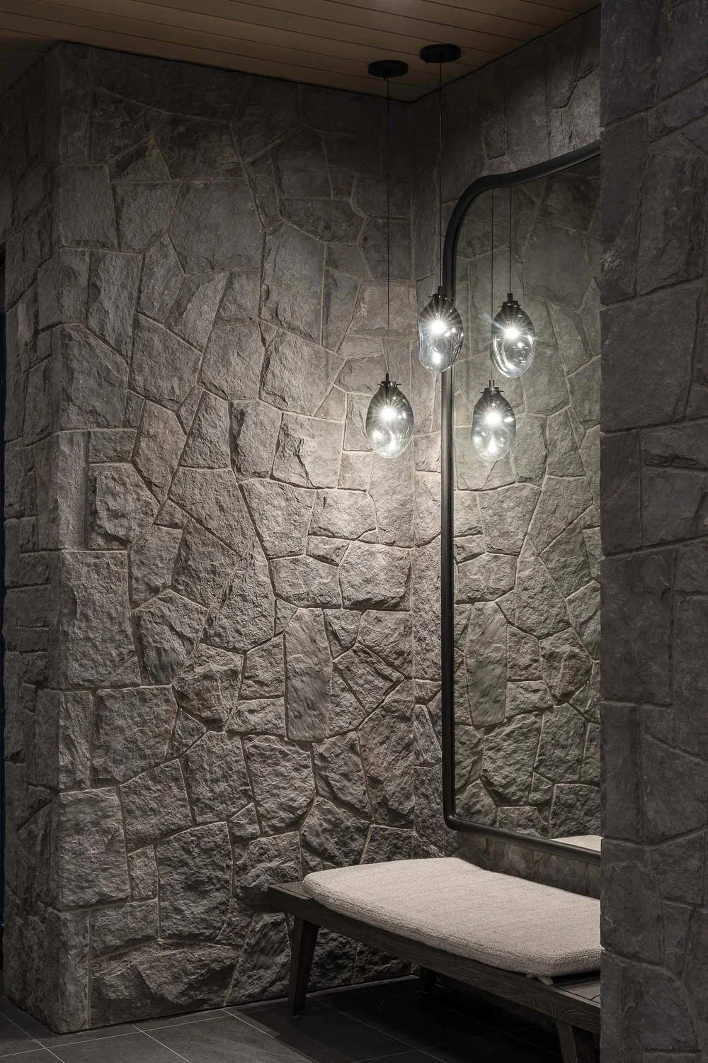 Bench in a stone lined alcove beneath a wall light with three glass globes