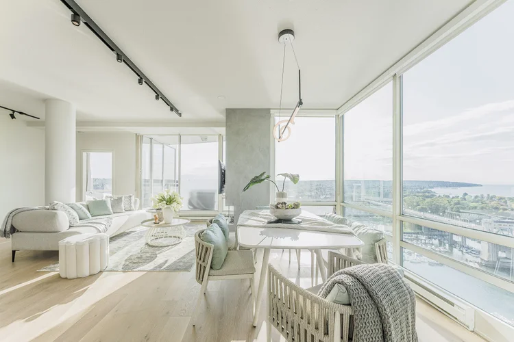 Open living and dining rooms behind corner glazing, a marina and the water far below
