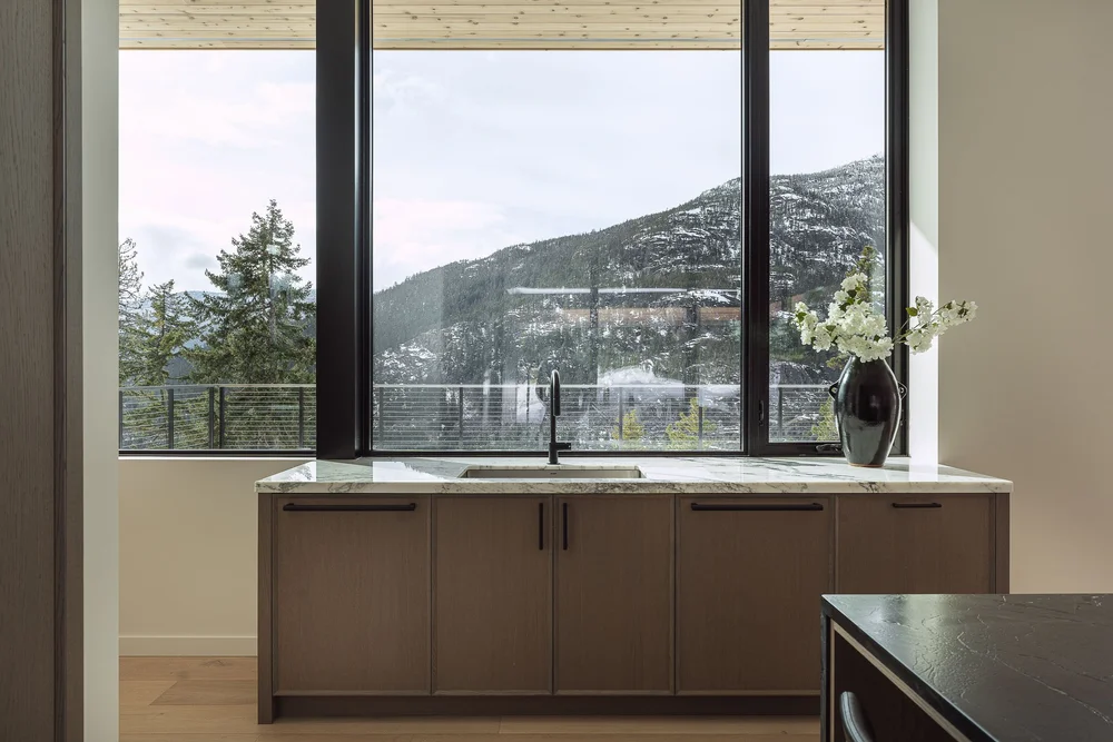 Prep counter in dark timber under a window, a vase on the stone top