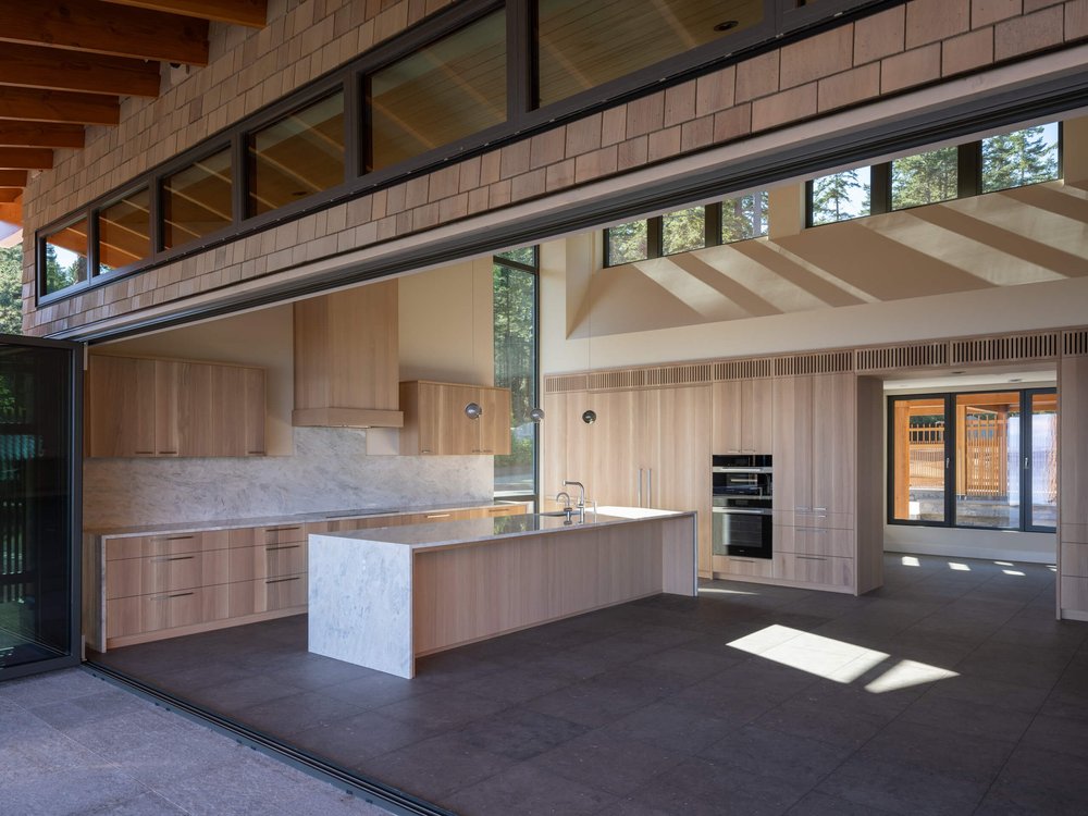 The kitchen seen through a wall of glass slid fully open, clerestory windows above