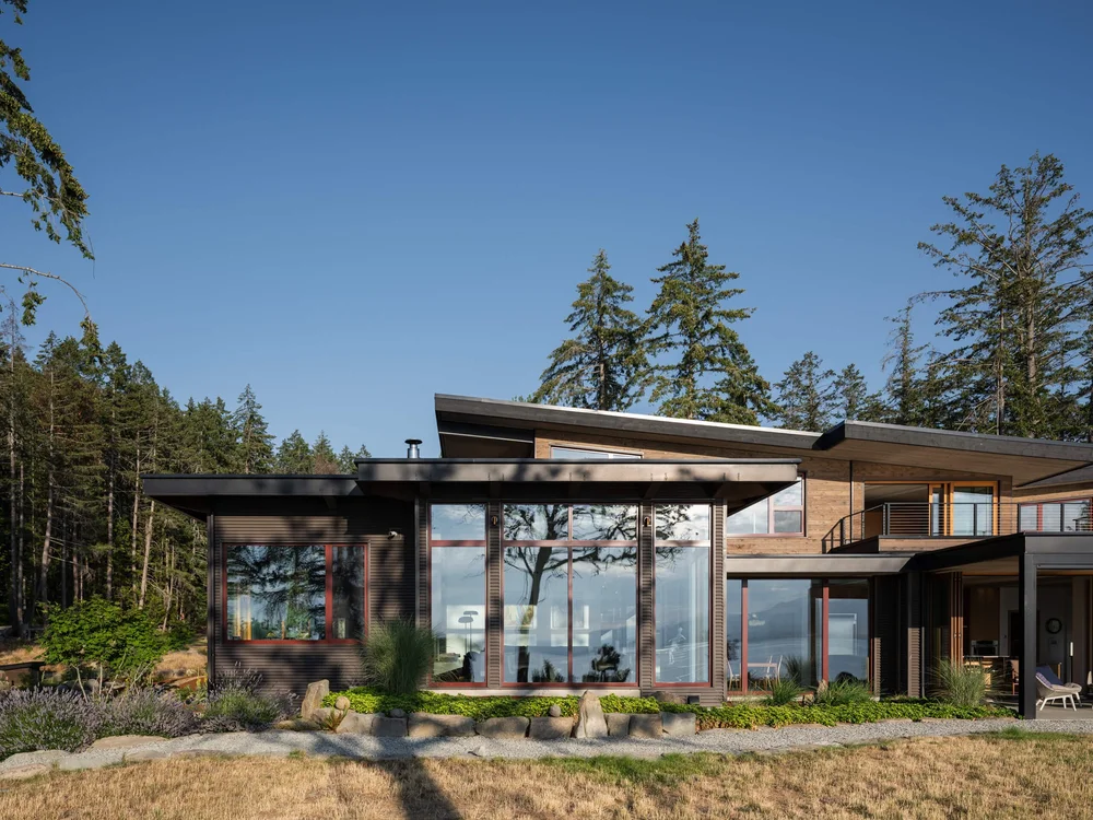 The house across dry grass, red framed glazing under a long low roof