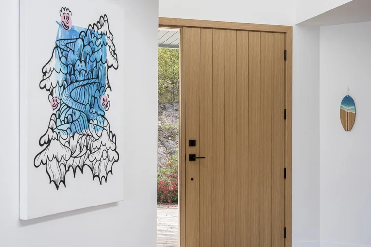 Entry with a pale wood plank front door standing open to a deck, a large framed drawing on the wall alongside