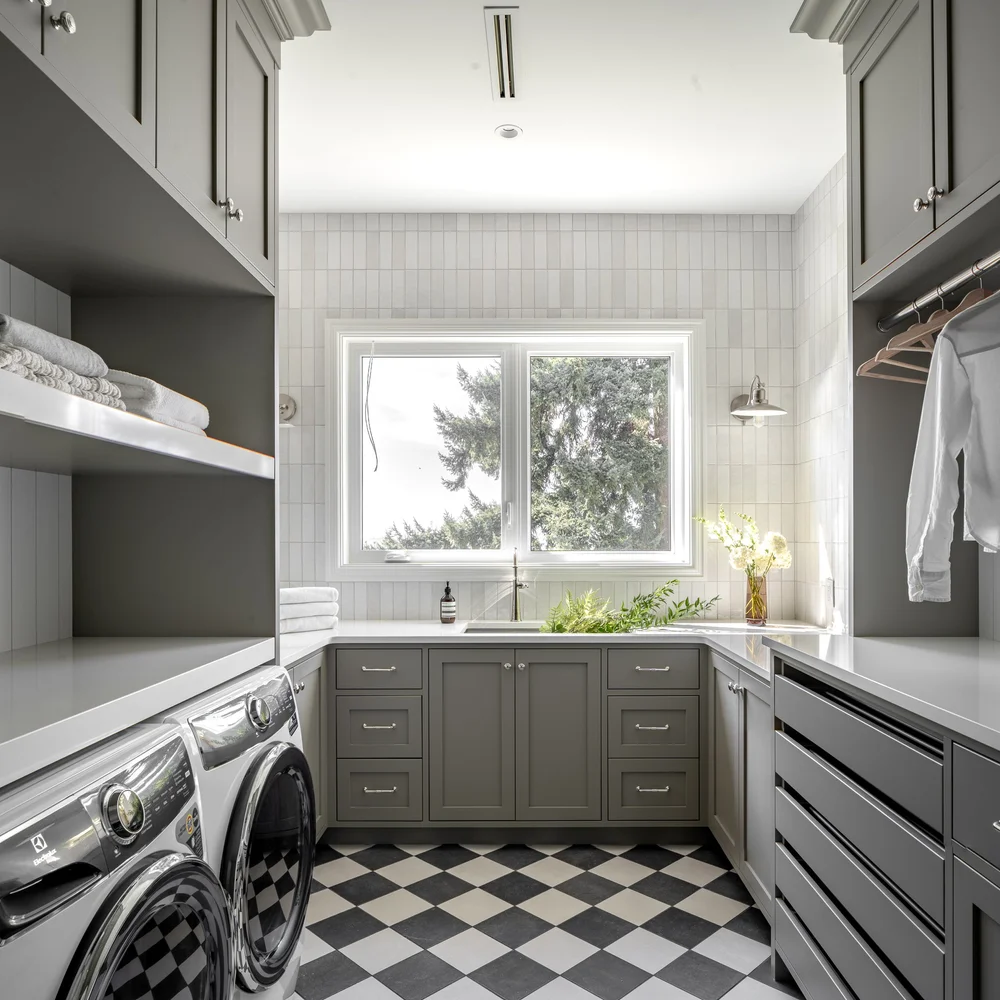Laundry room in dark grey green cabinetry with a window over the sink and a hanging rail