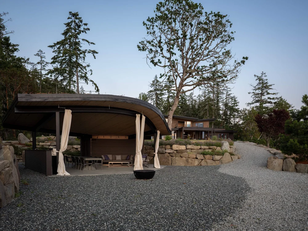 Pavilion and house at dusk, a bare tree rising between them above the gravel court